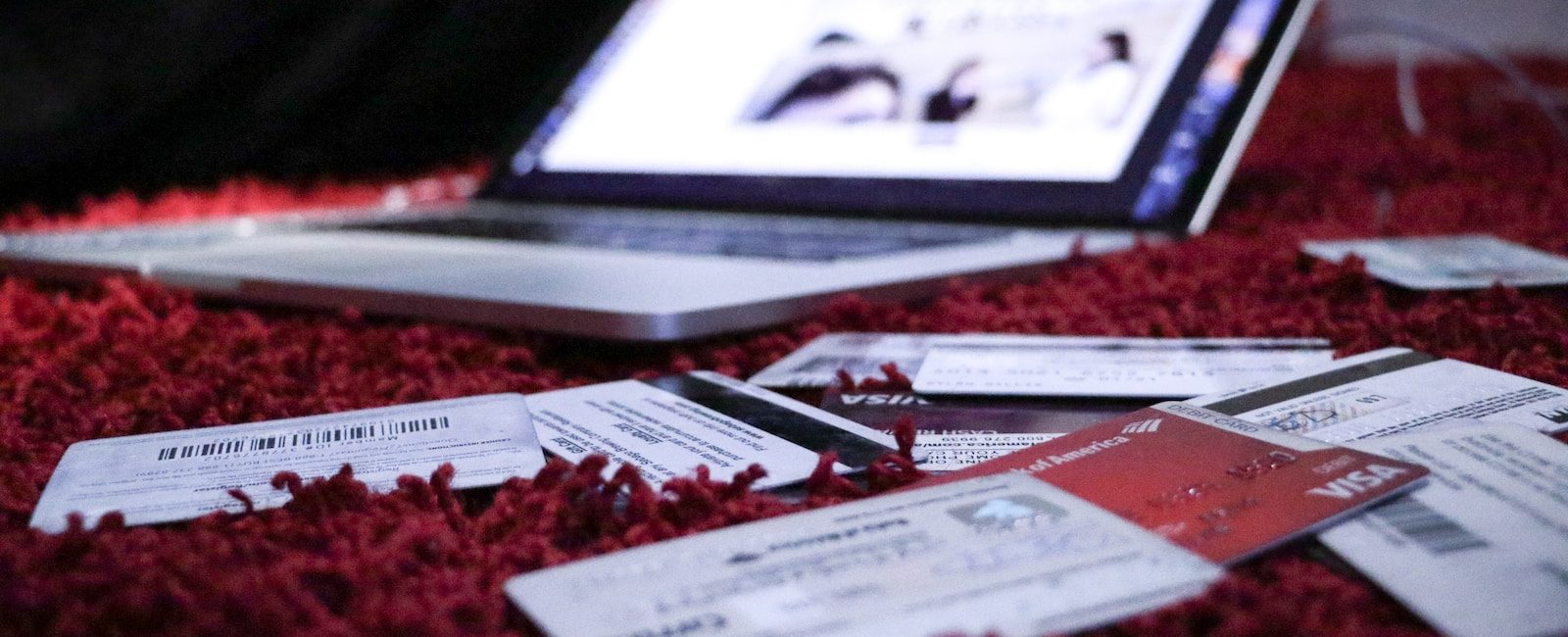 Laptop on red carpet surrounded by various credit cards and documents, depicting online shopping or financial planning