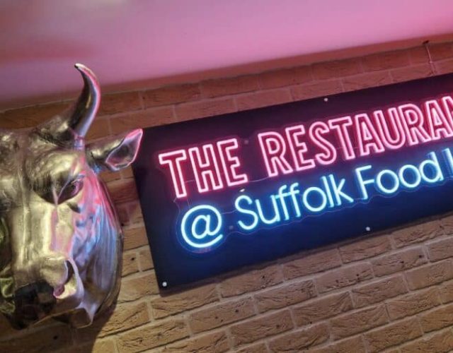 Neon sign reading The Restaurant Suffolk Food Hall next to a bull head sculpture on a brick wall