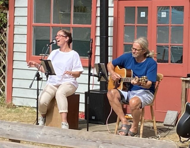 Musicians performing outdoors with guitar and microphone in front of vintage building