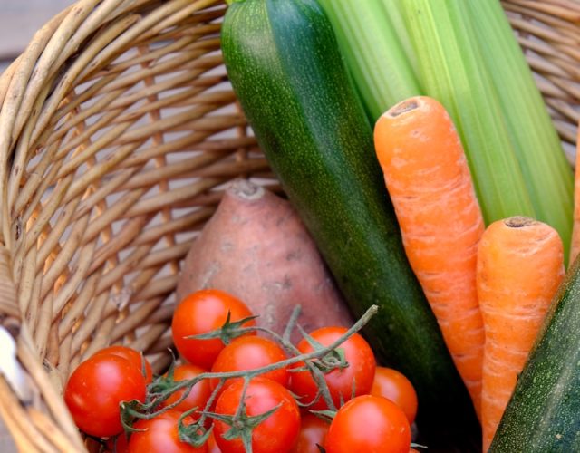 Basket of fresh vegetables and fruits including tomatoes, carrots, courgettes, celery, orange satsumas and sweet potatoes
